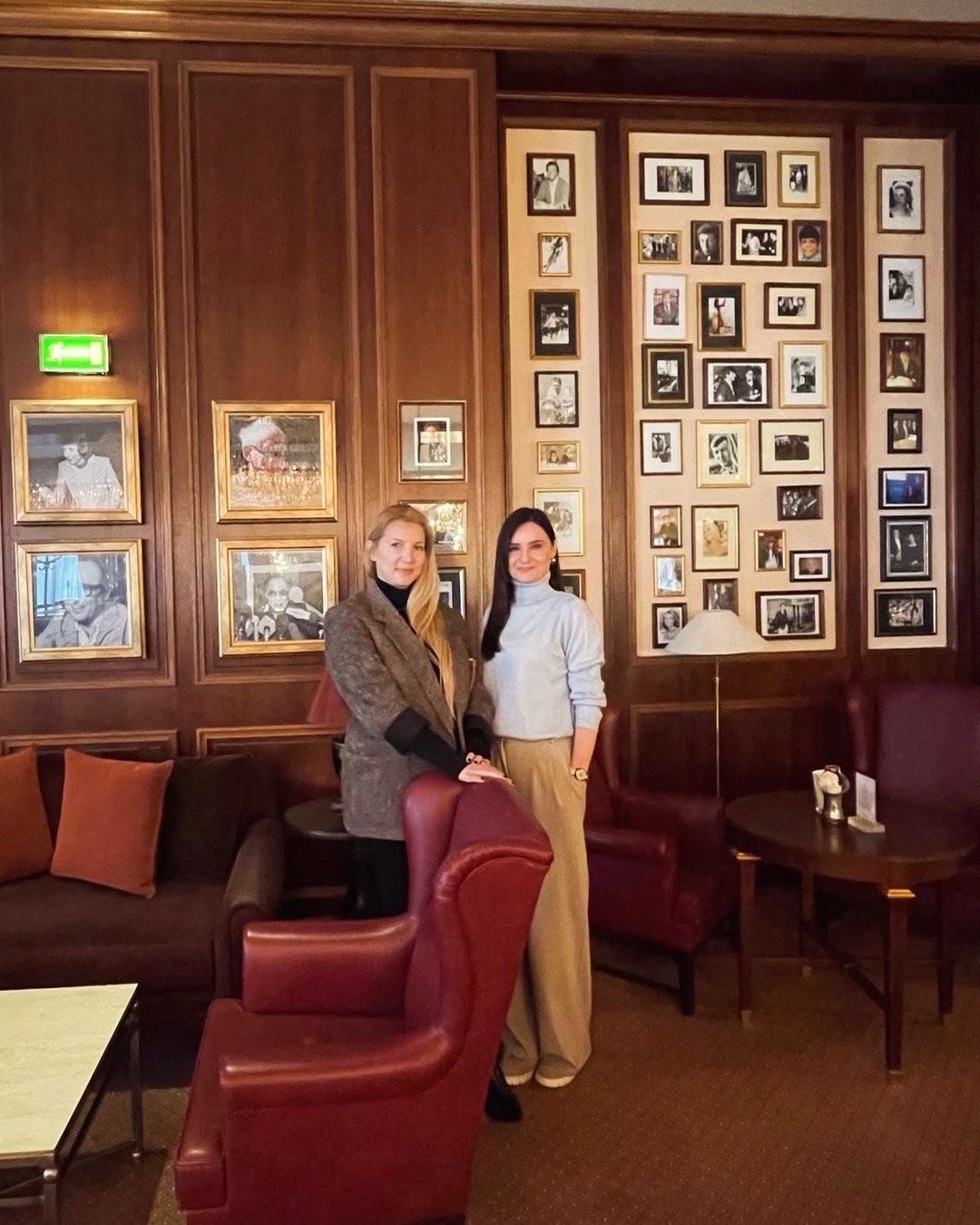 Marija and Maja standing side by side in a wood-panelled lounge hung with framed photographs