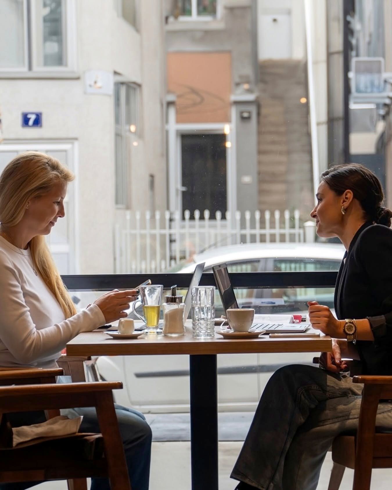 Maja and Marija, the co-founders, working together at a café table with a laptop and coffee in daylight